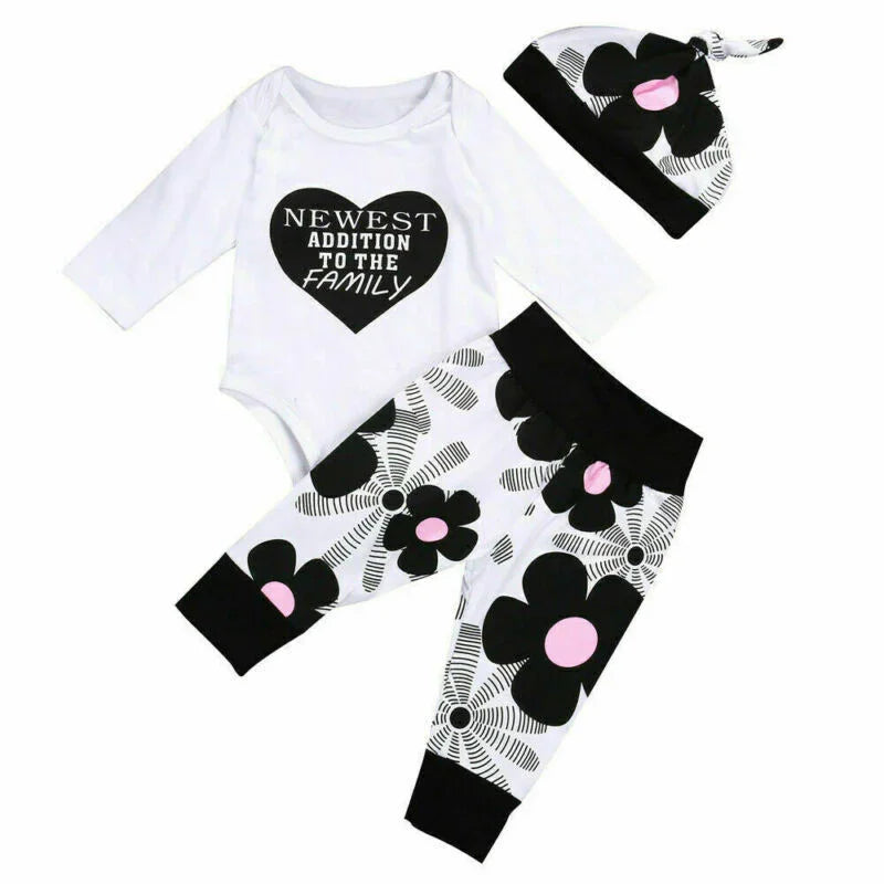 Baby clothes set with white long-sleeve onesie featuring 'Newest Addition to the Family' text and black floral leggings and matching hat