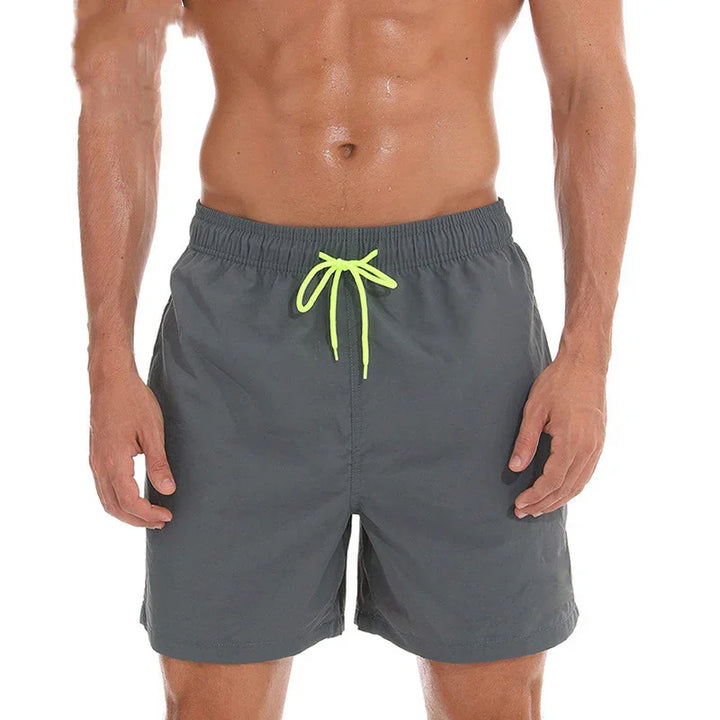 Men's gray swim trunks with neon yellow drawstring worn by a fit male model