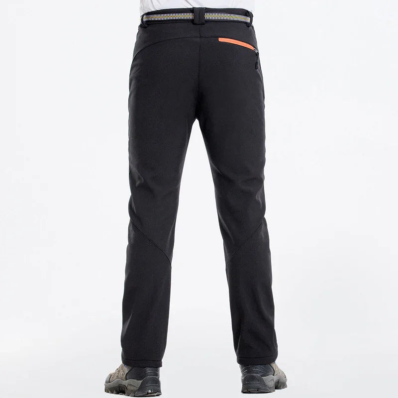 Back view of black hiking pants with zipper pocket and striped belt, worn with outdoor shoes