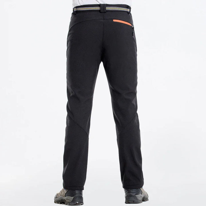 Back view of black hiking pants with zipper pocket and striped belt, worn with outdoor shoes