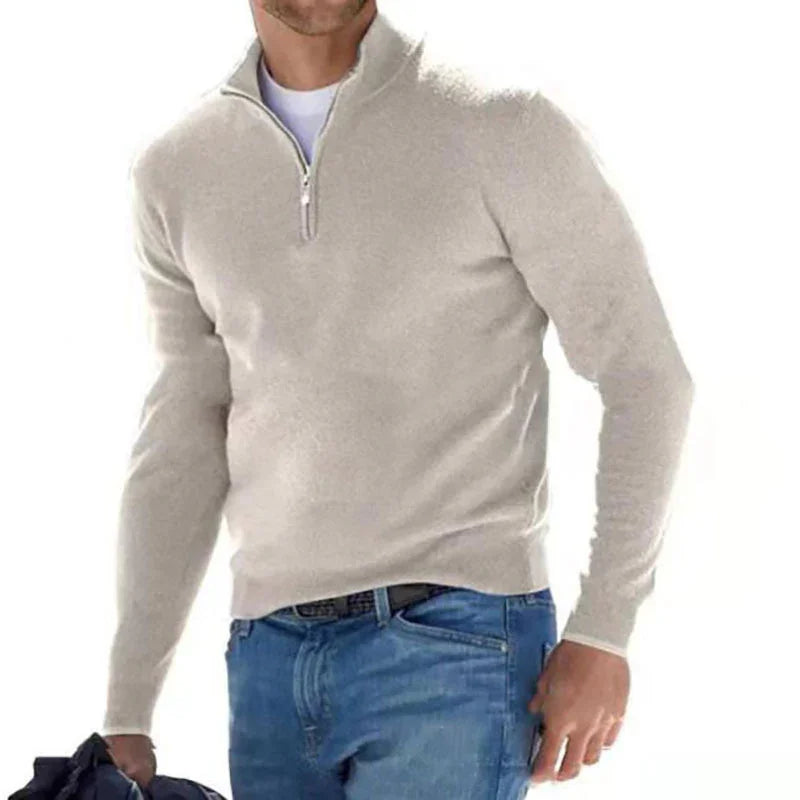 Man wearing light gray quarter-zip sweater and blue jeans holding a dark jacket