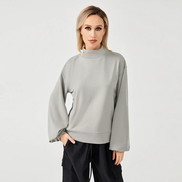 Woman wearing light gray turtleneck sweater with balloon sleeves and black cargo pants on white background