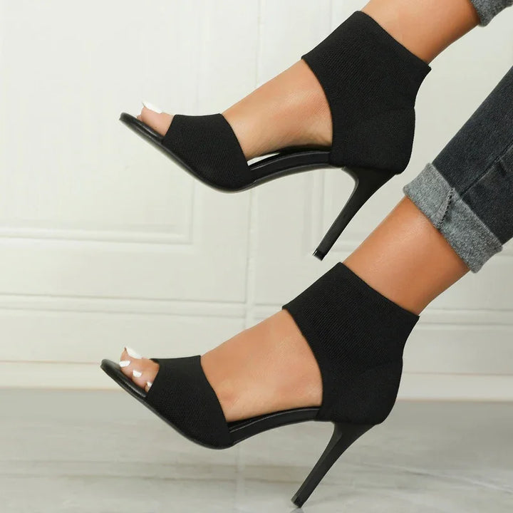 Woman wearing black open-toe high heel ankle booties with slim heels and cuffed dark jeans