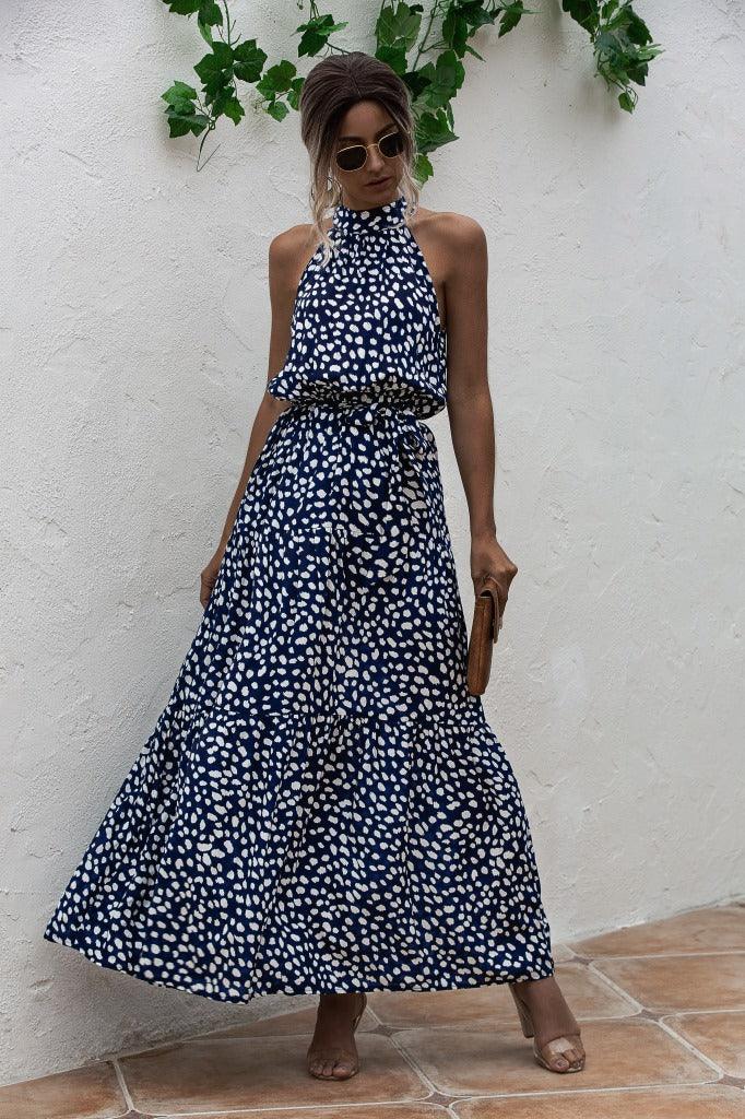Woman wearing navy blue and white polka dot halter neck maxi dress with sunglasses and clutch