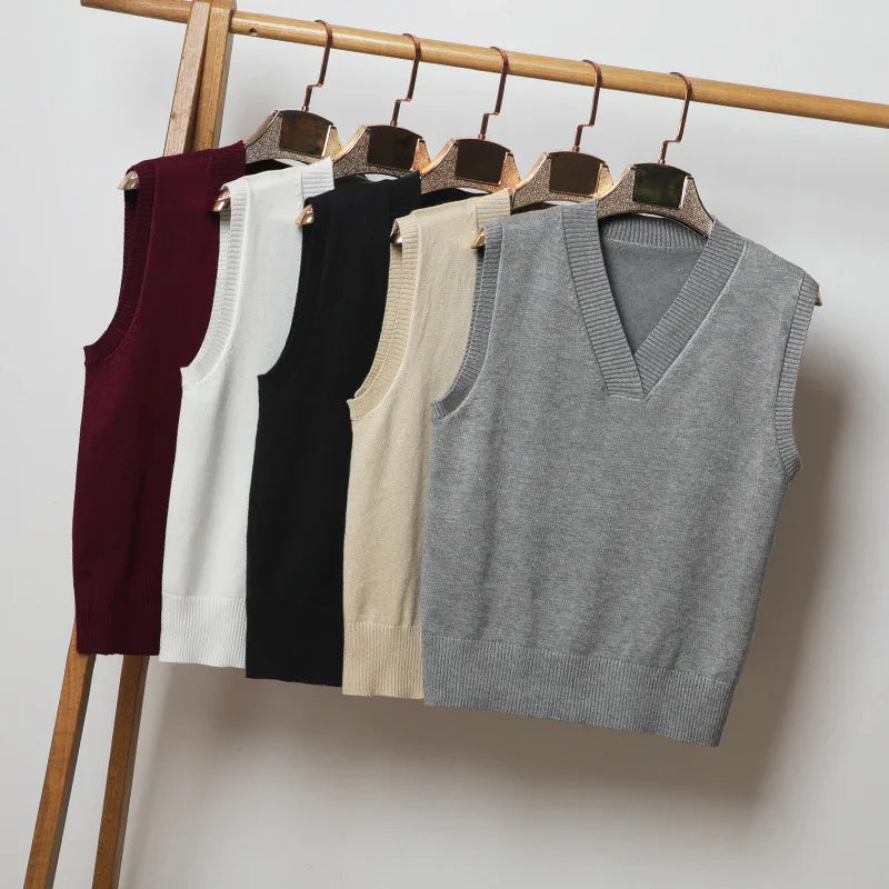 Five sleeveless knitted sweater vests in burgundy, white, black, beige, and gray on wooden hangers