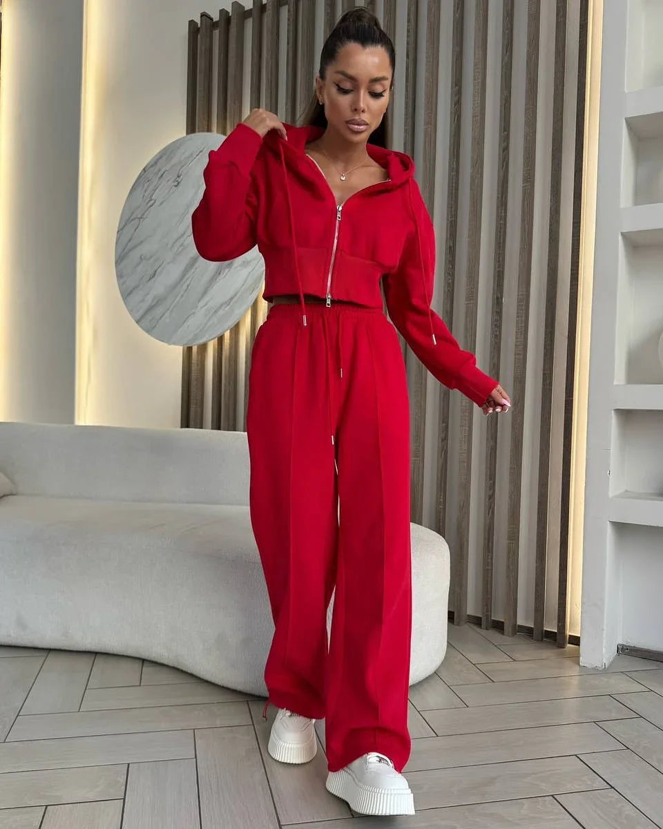 Woman wearing a red zip-up hoodie and matching wide-leg pants with white platform sneakers in a modern indoor setting