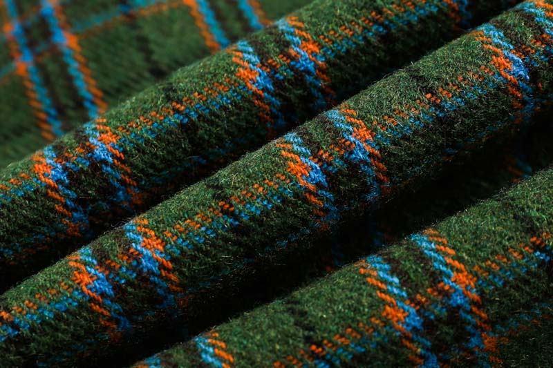 Close-up of green wool fabric with orange and blue plaid pattern, soft textured textile