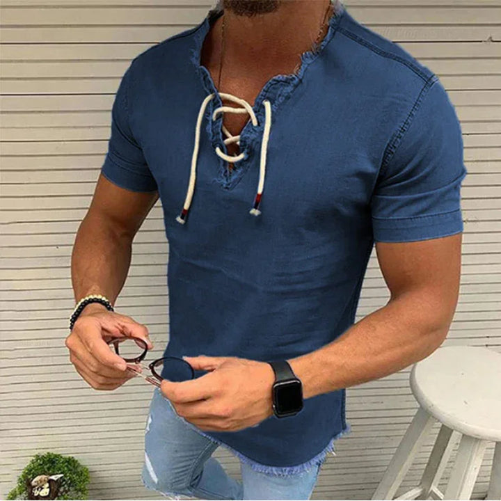 Man wearing distressed blue lace-up short sleeve t-shirt and ripped jeans holding sunglasses