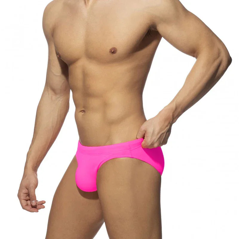 Muscular man wearing bright pink swim briefs against white background