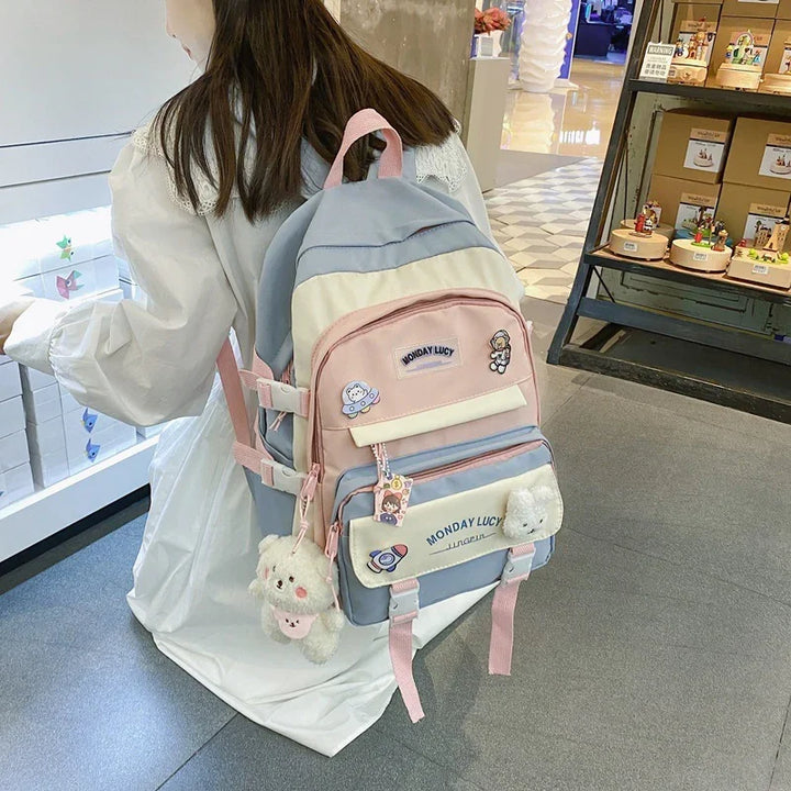 Girl wearing pastel pink and blue Monday Lucy backpack with bear keychains and cartoon patches indoors
