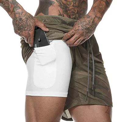 Tattooed man wearing green camo shorts with inner white pocket holding a phone