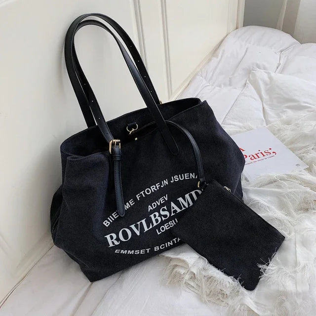 Black canvas tote bag with adjustable straps and matching small pouch on white bed with book