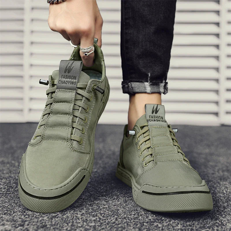 Close-up of olive green casual sneakers, one worn and one held by a hand with rings, on grey surface