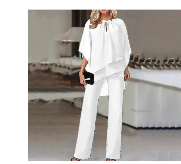 Woman in stylish white asymmetrical blouse and wide-leg trousers holding black clutch in modern indoor setting