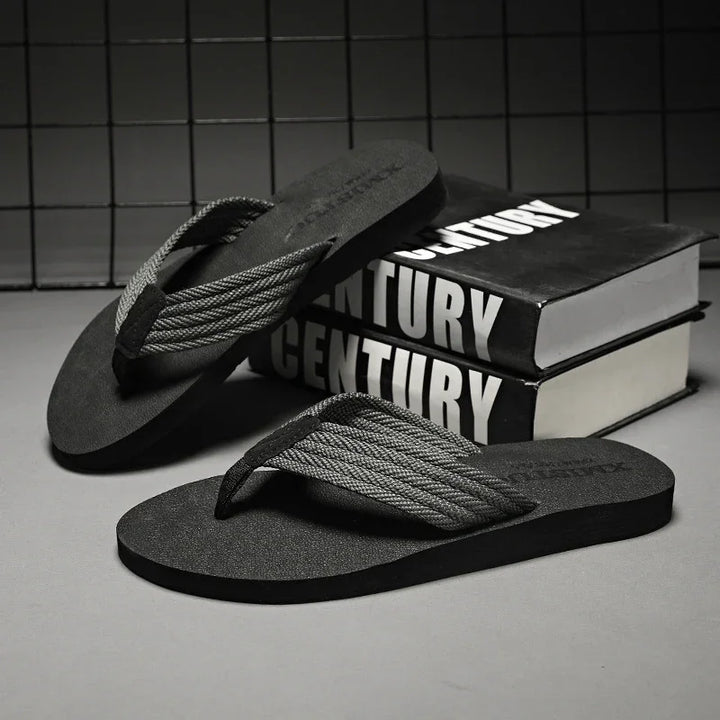 Black flip-flops with braided gray straps placed near stacked books with "CENTURY" text on covers