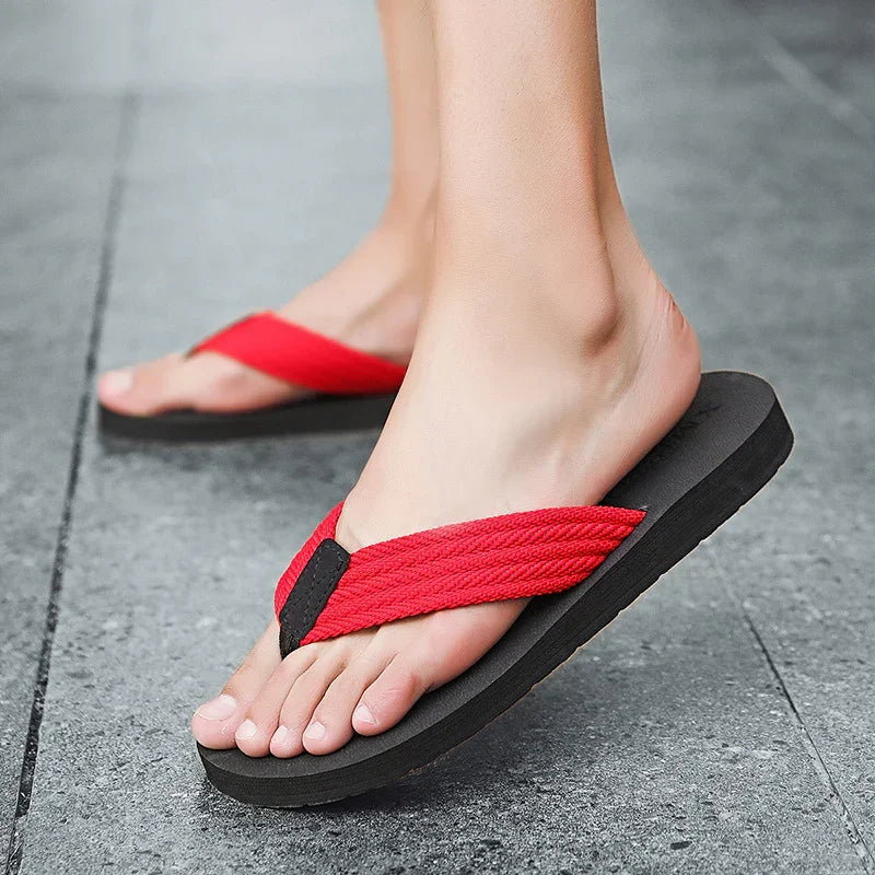 Feet wearing black sole flip-flops with red fabric straps on grey pavement