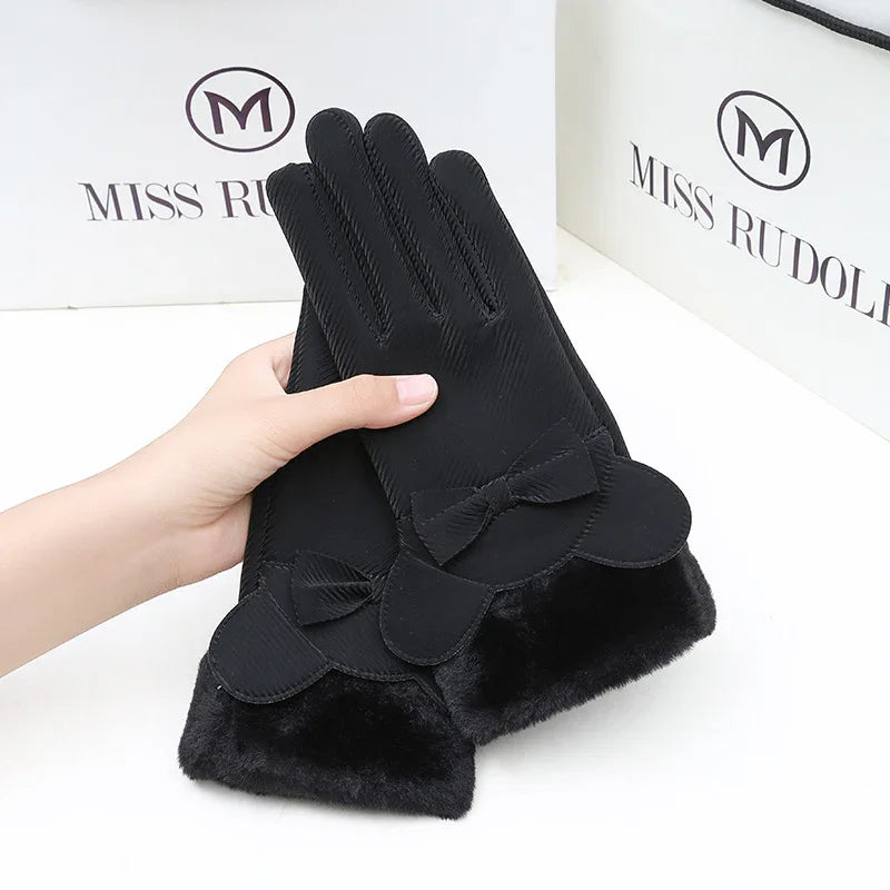 Black women's winter gloves with bow detail and faux fur cuffs held by hand, Miss Rudolph packaging in background