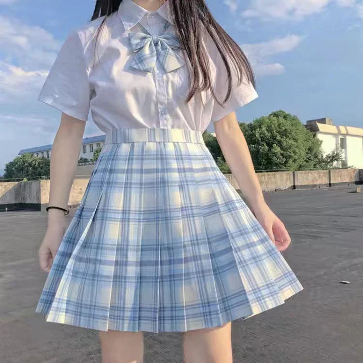 Woman wearing blue and white plaid pleated skirt with white short-sleeve shirt and matching bow outdoors