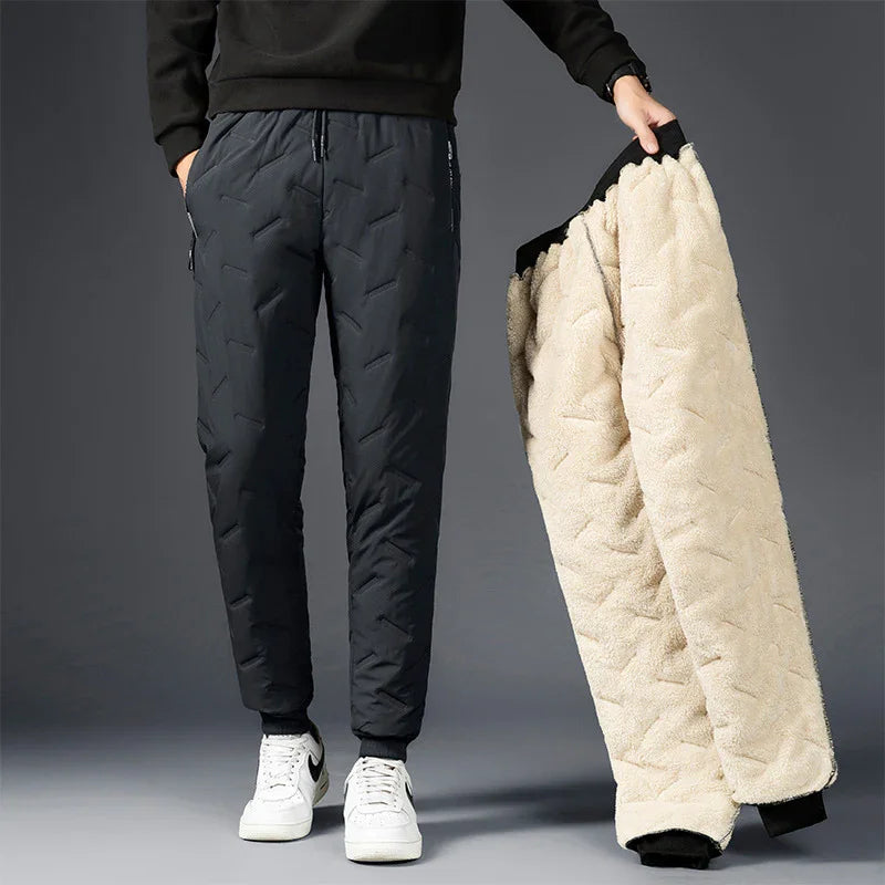 Man wearing black quilted jogger pants holding beige fleece-lined pants against gray background
