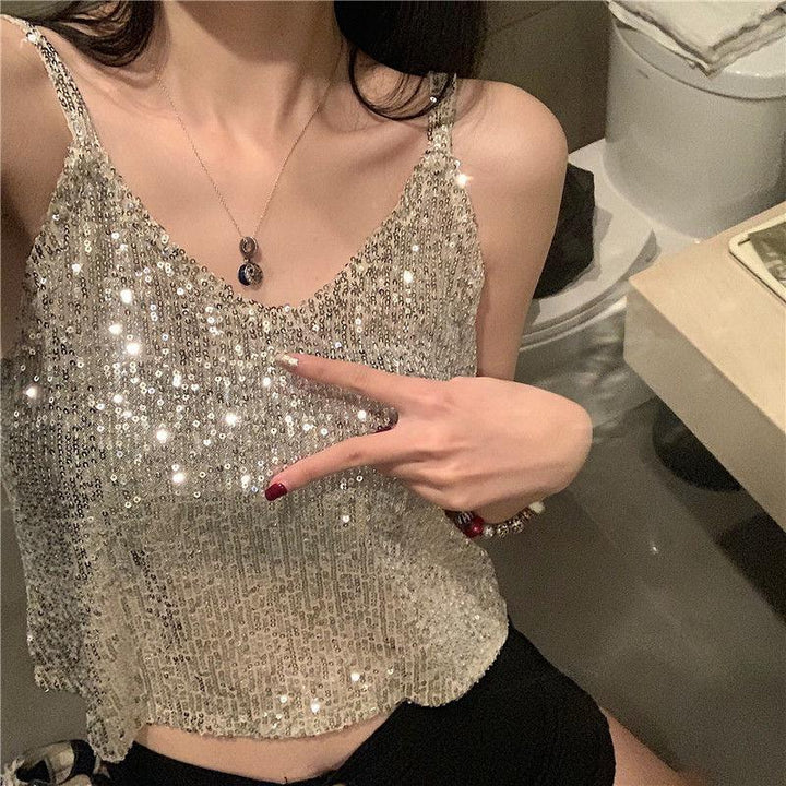 Woman wearing a sparkly sequin silver tank top and black shorts, posing with a peace sign indoors
