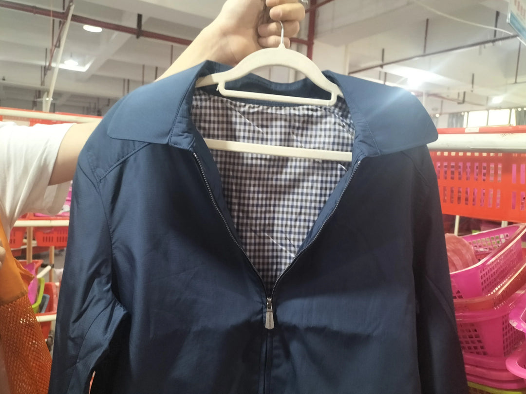 Hand holding navy blue jacket with checkered lining on white hanger in indoor market
