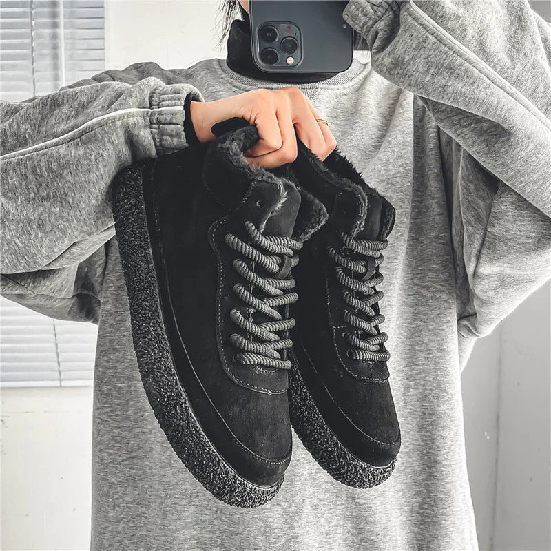 Person in grey sweatshirt holding black winter boots with fuzzy lining and textured soles