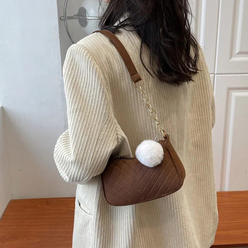 Woman wearing cream ribbed jacket holding brown quilted shoulder bag with white pom pom charm