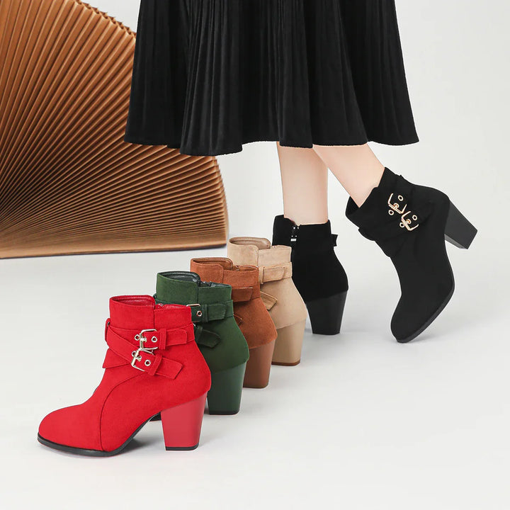 Row of stylish suede ankle boots in red, green, brown, beige, and black on white floor