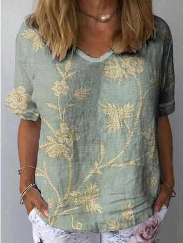 Woman wearing a sage green textured short-sleeve blouse with beige floral embroidery and light patterned pants