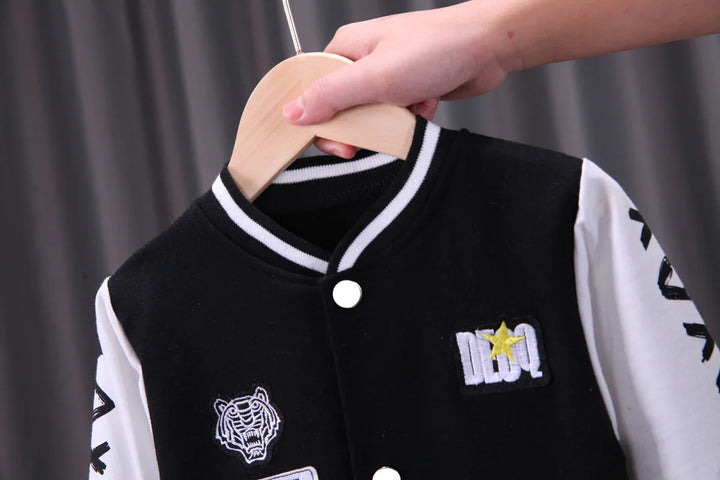 Hand holding black and white varsity jacket with tiger patch and star emblem on hanger