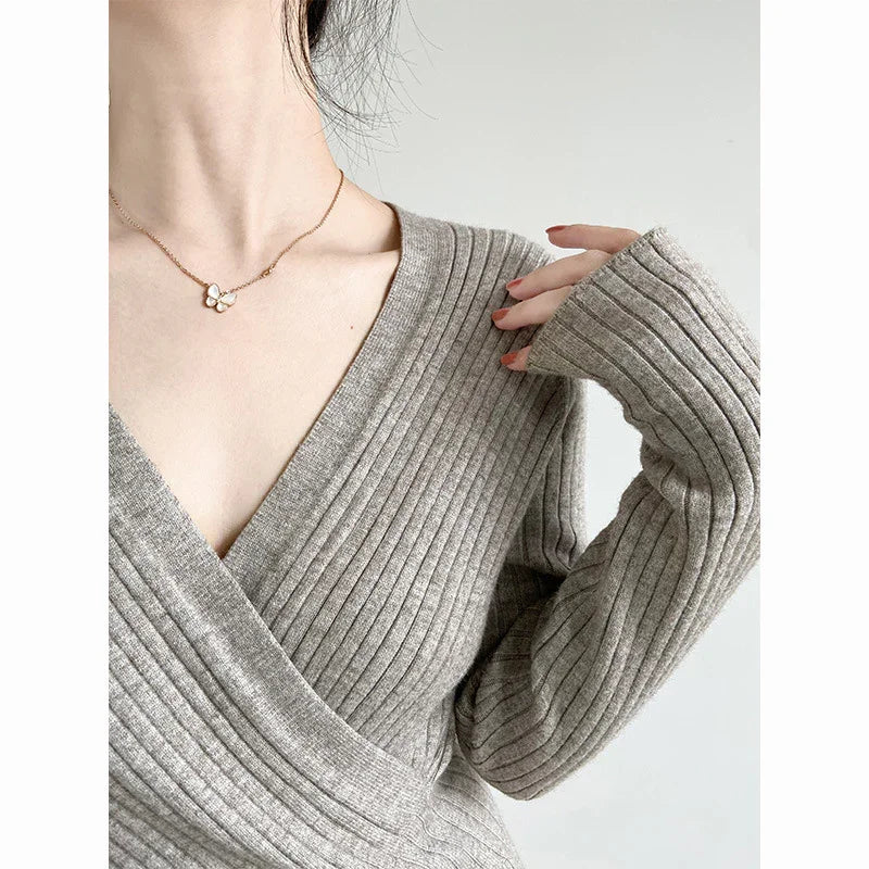 Woman wearing gray ribbed knit wrap sweater and gold butterfly pendant necklace