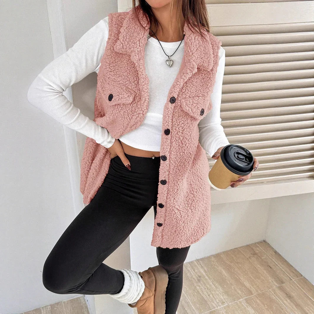 Woman wearing pink sherpa fleece vest with black buttons, white crop top, black leggings, and tan boots holding coffee cup