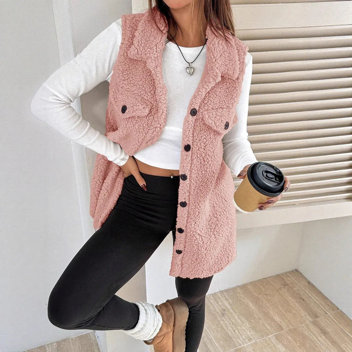 Woman wearing pink sherpa fleece vest with black buttons, white crop top, black leggings, and tan boots holding coffee cup