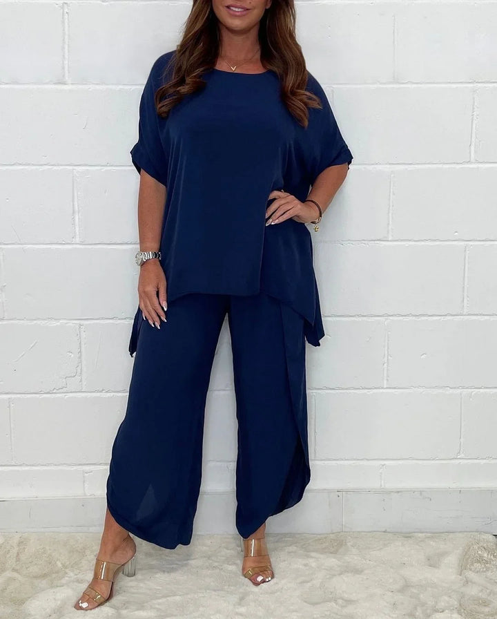 Woman in navy blue loose top and wide-leg pants standing against white brick wall