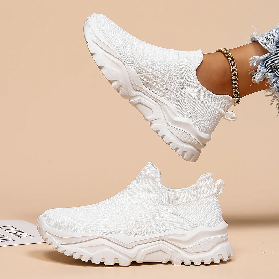 Pair of white slip-on knit sneakers with chunky sole, worn with ripped jeans and gold anklet