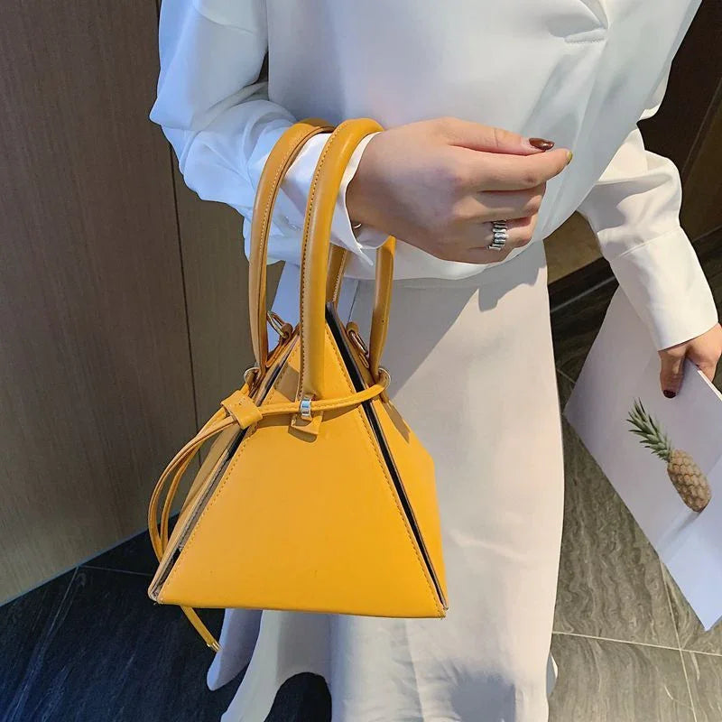 Woman wearing white outfit holding a yellow pyramid-shaped handbag with dual handles