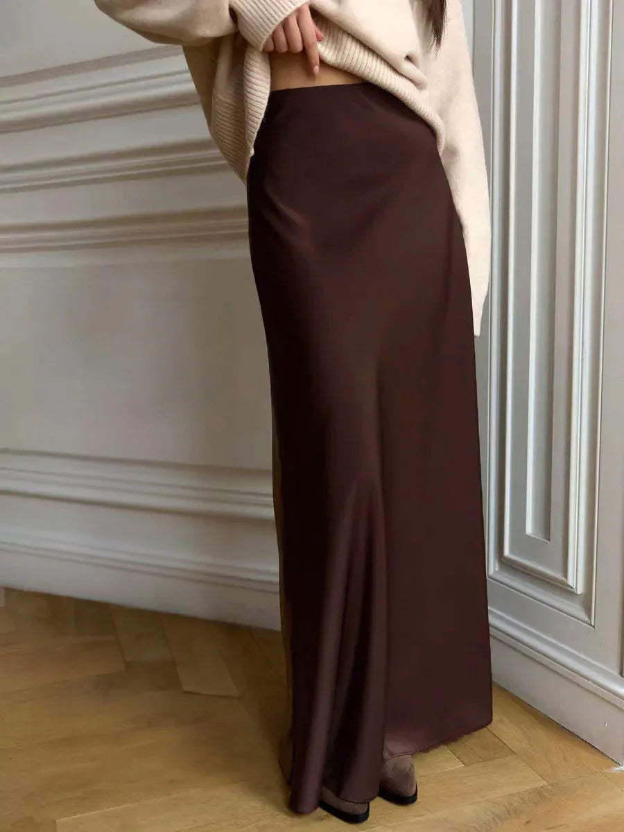 Woman wearing a chocolate brown satin maxi skirt with beige sweater in a room with white paneled walls