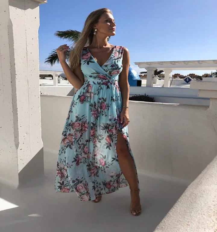 Woman in blue floral sleeveless maxi dress with slit posing outdoors on white terrace under clear sky