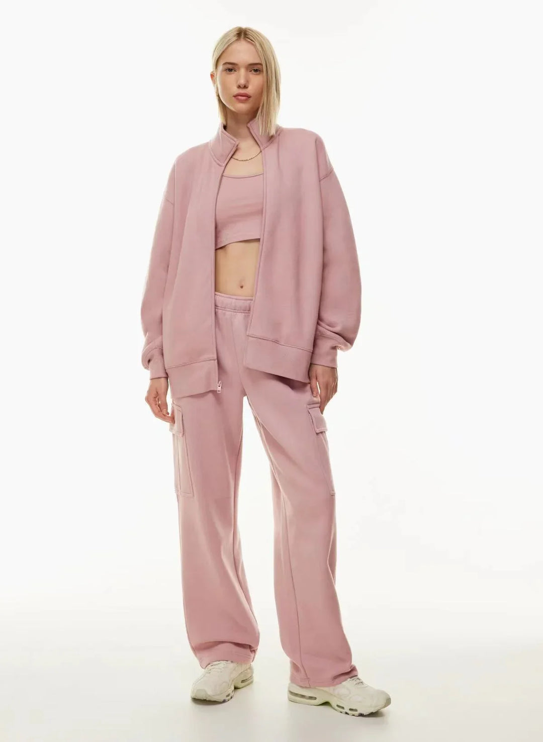 Woman in light pink lounge set with cargo pants, open jacket, crop top, and white sneakers.