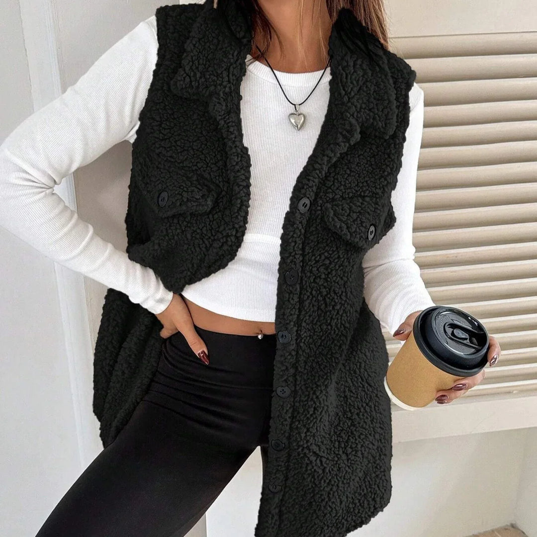 Woman wearing black sherpa fleece vest over white long sleeve crop top with black leggings, holding coffee cup
