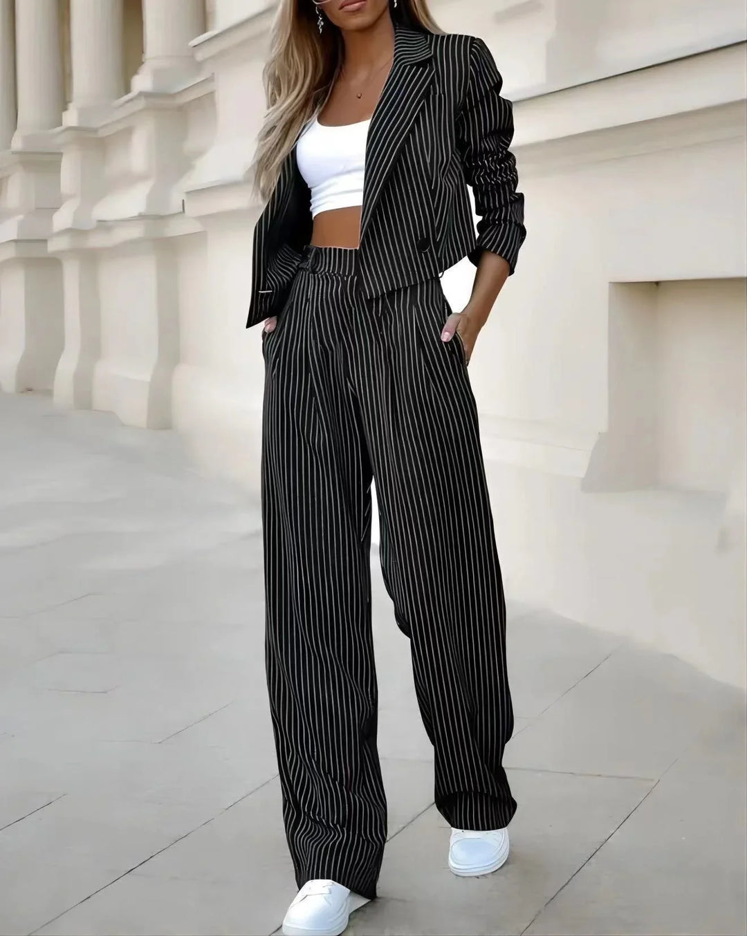 Woman wearing black pinstripe wide-leg trousers and matching cropped blazer with white crop top and sneakers