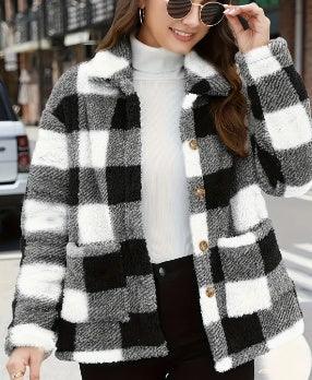 Woman adjusting sunglasses wearing a black and white checkered wool jacket over a white turtleneck sweater on a city street