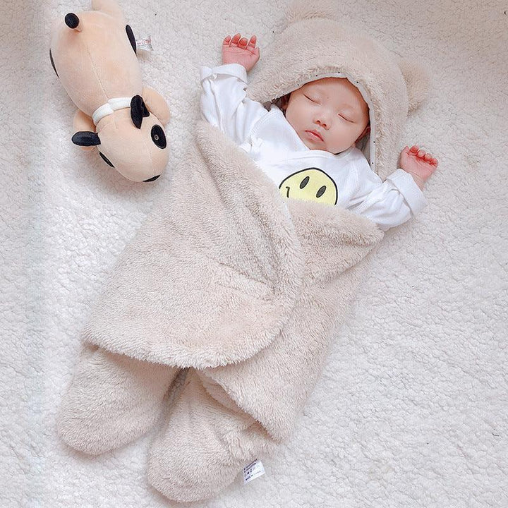 Sleeping baby wrapped in cozy beige hooded blanket on soft white carpet with plush dog toy