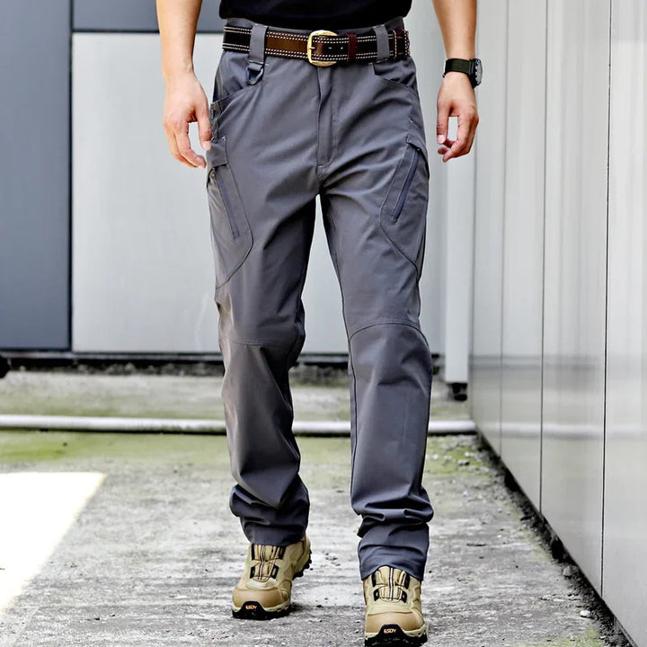 Man wearing gray tactical cargo pants with brown belt and beige hiking boots walking outdoors