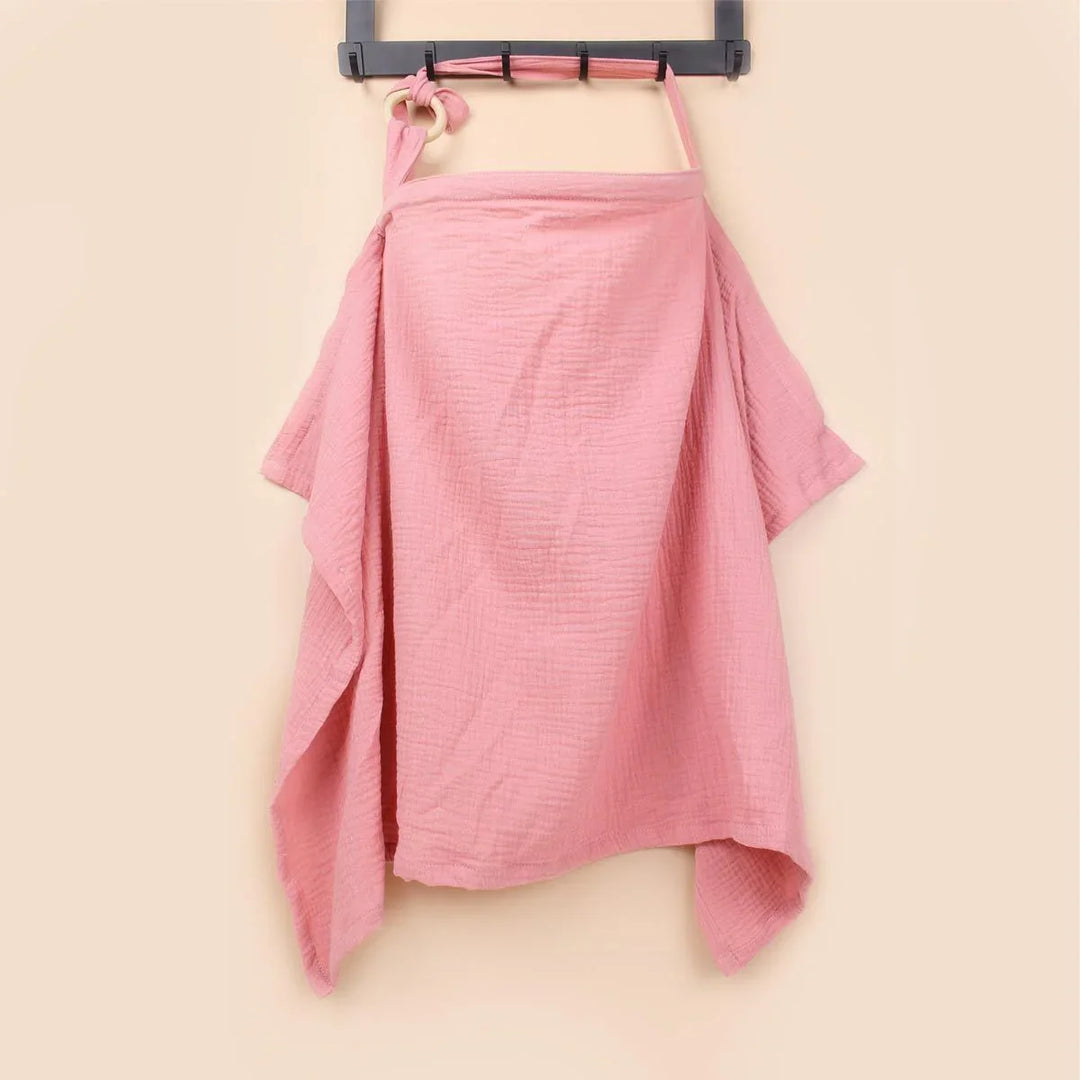 Soft pink muslin nursing cover with wooden ring hanging on black hanger against beige wall