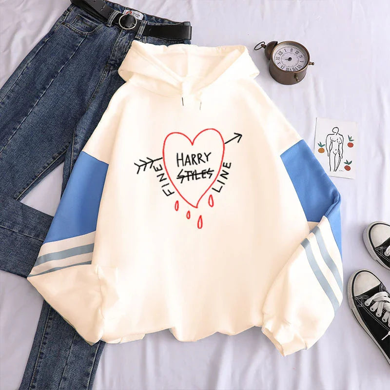 Cream hoodie with blue sleeve stripes and red heart graphic saying 'Harry Styles Fine Line' paired with jeans and sneakers