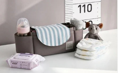 Brown baby organizer with bib, bottle, socks, cloth, diapers, and wipes on white surface
