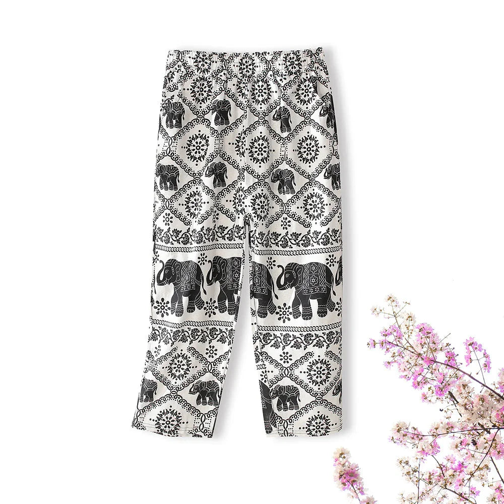 Black and white elephant print boho pants laid flat with delicate pink flowers nearby