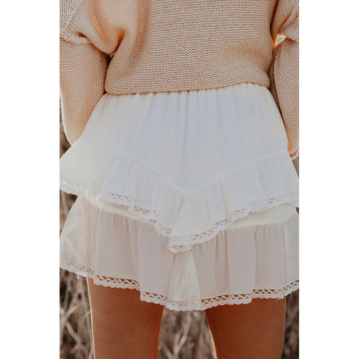 Woman wearing white ruffled mini skirt and beige knit sweater in outdoor setting