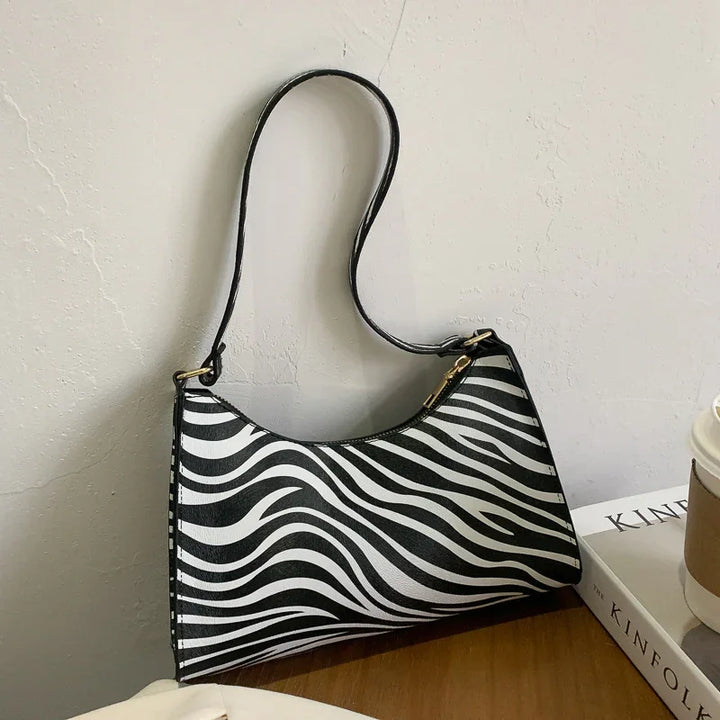 Black and white zebra print shoulder bag on wooden surface next to books and coffee cup